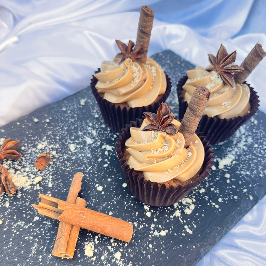 Three cupcakes with frosting and star anise on a dark surface with cinnamon sticks and star anise.