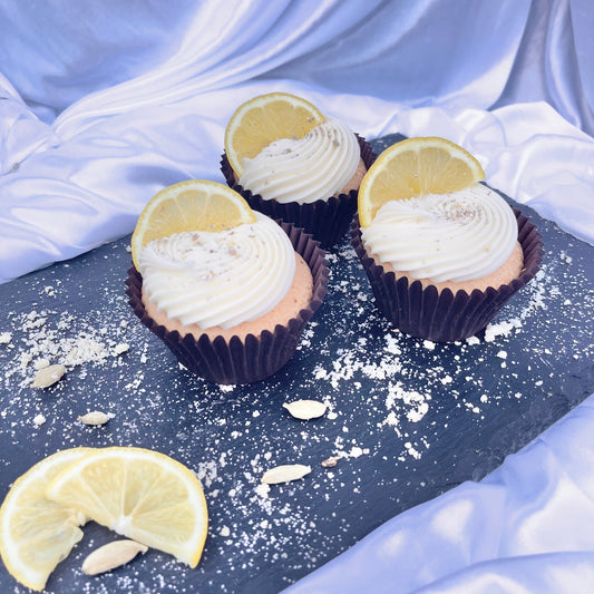 Cupcakes with lemon slices and white frosting on a dark surface with a light fabric background.