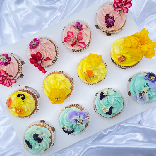 A selection of beautifully decorated cupcakes with a variety of colorful icing and edible floral decorations.