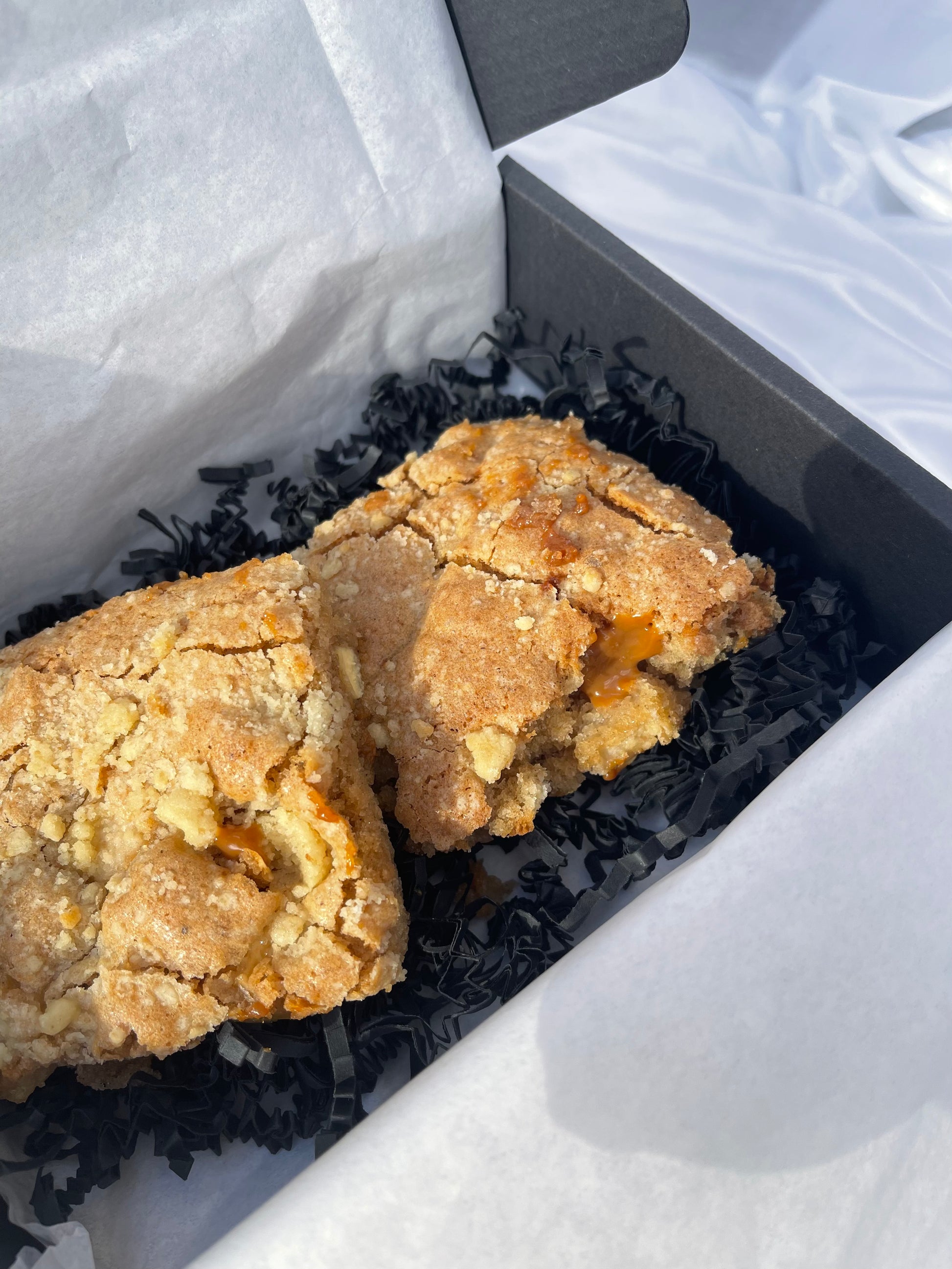 Two pieces of fried chicken in a black postal container with black shredded paper.